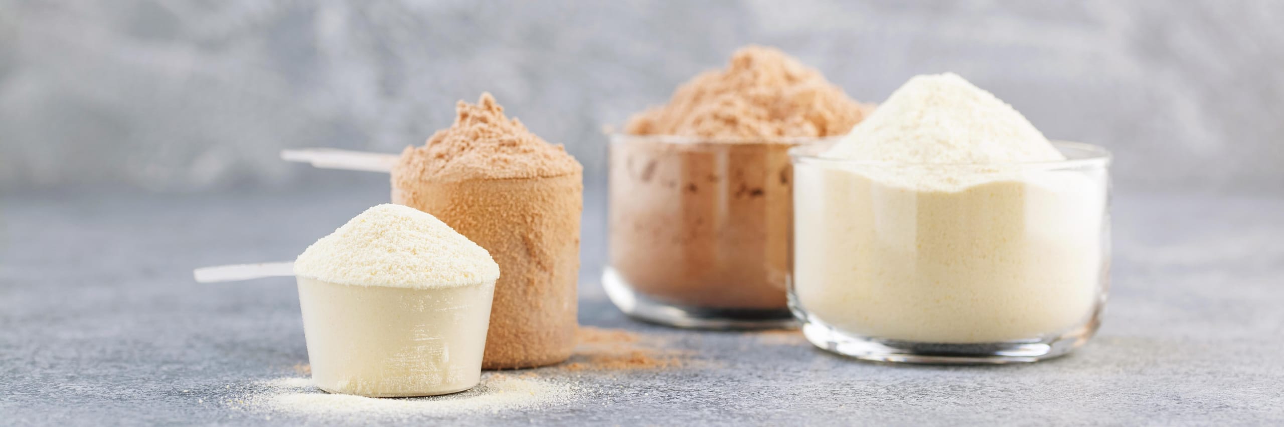 Dry mixture for preparation of sporting or dietary drink. Sports nutrition, fitness diet and food concept - protein shake powder on grey background. Banner